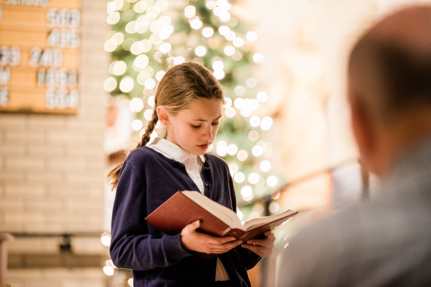 girl reading Bible in front of a Christmas tree